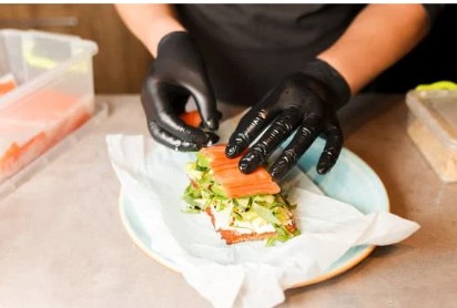 persons hands wearing black gloves preparing food