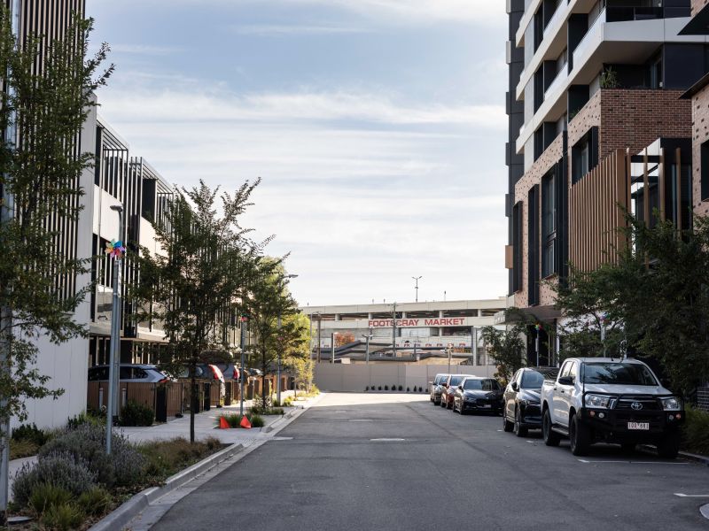 Residential street lined with modern apartments and townhouses, parked cars and street trees, with Footscray Market visible at the end of the road.